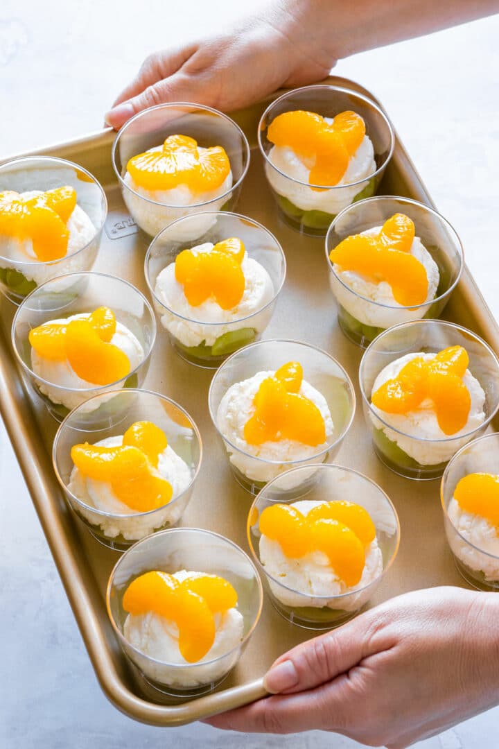 Tray of layered dessert cups with green grapes, creamy white layer and mandarin orange segments, ready to chill and serve.