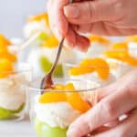 Close-up of spooning a layered party dessert cup with green grapes, creamy mascarpone filling and mandarin orange segments, inspired by Irish flag colors.